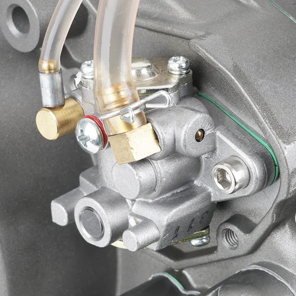 Close-up of a small engine carburetor with fuel hoses, brass fittings, and clamps visible on a gray engine block.