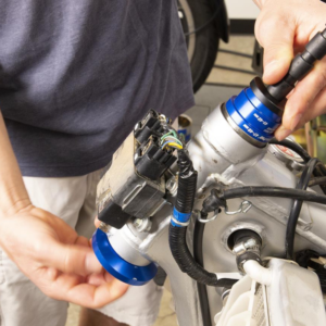 Motion Pro – Outil de Montage pour Roulement de Direction - Creations Mx Factory Person installing a blue anodized connector/fitting on a metal engine part, with wiring harness nearby.